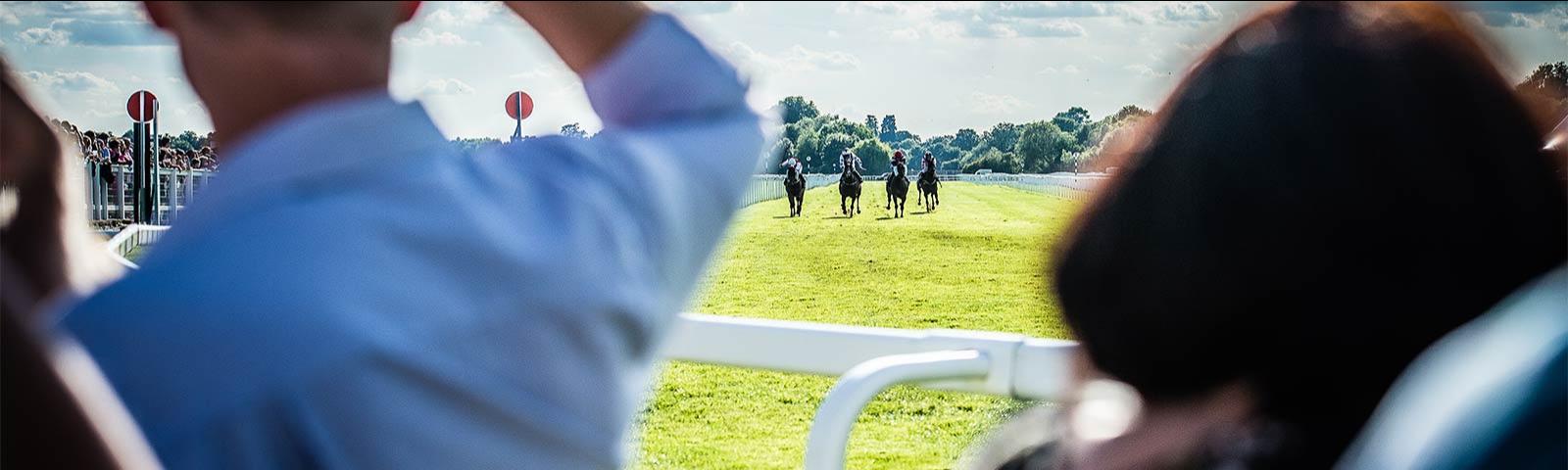 Jockeys racing at Windsor Racecourse with racegoers looking on.