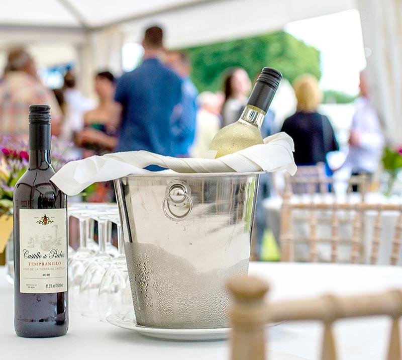 A bottle of red wine on the table and a bottle of white in a bucket of ice.