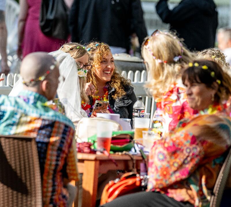 Members of a stag and hen party dressed up in colourful flower outfits sit round a table at Windsor Races.