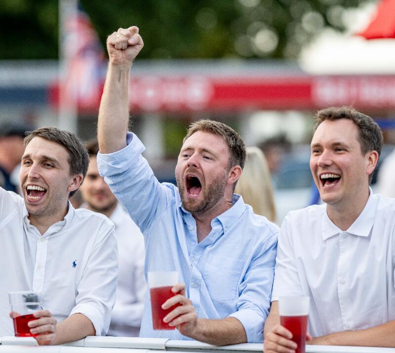 Three race goers cheering on their horse from the trackside at Windsor Races